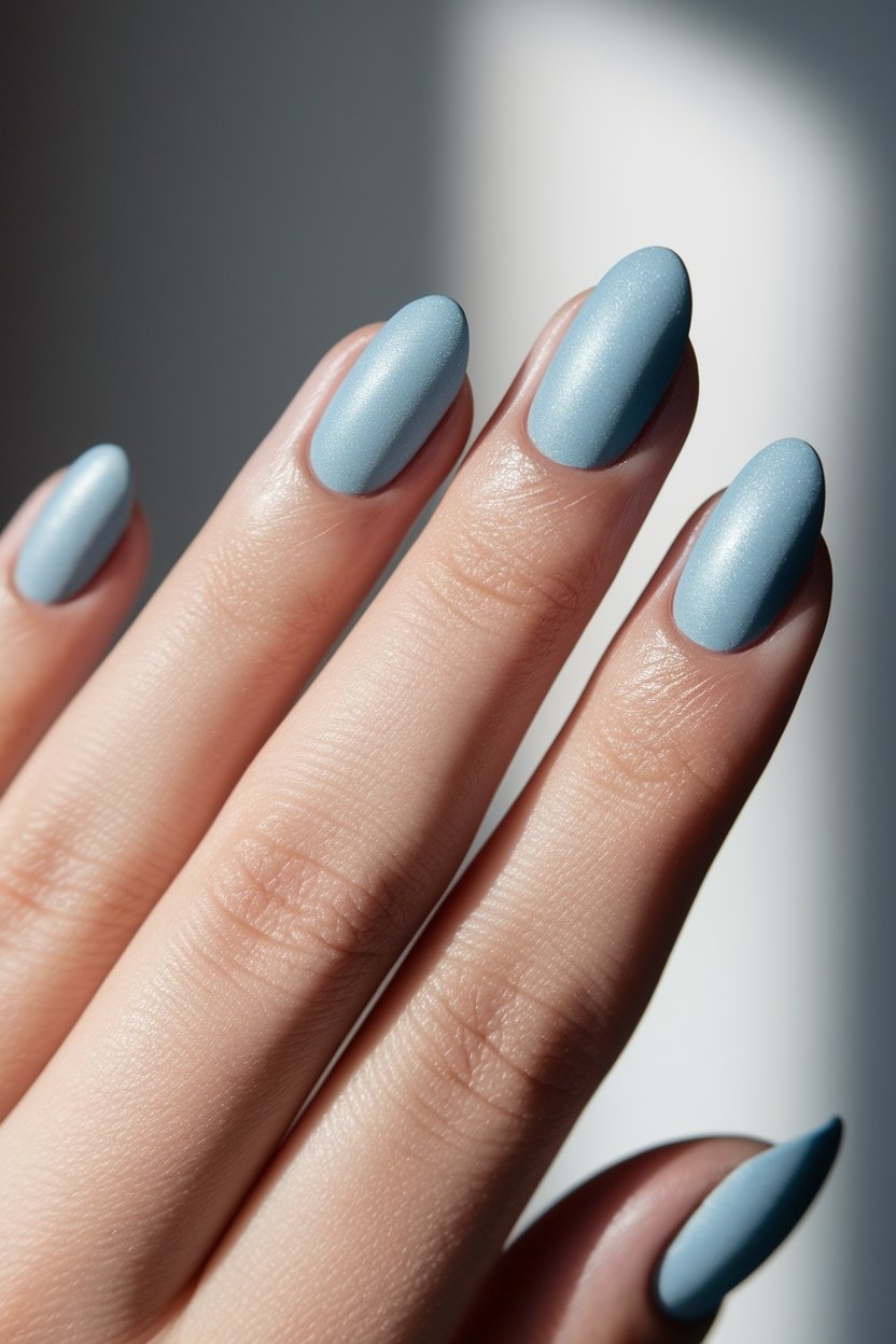 Close-up of hand with light blue, almond-shaped nails, showcasing elegant manicure in natural lighting.