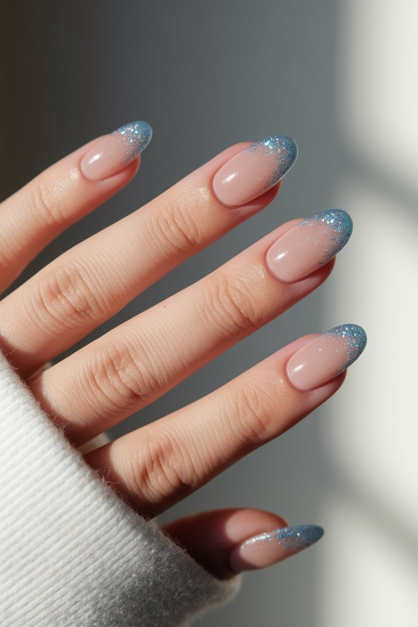 Close-up of hand with glittery blue French manicure under soft lighting.