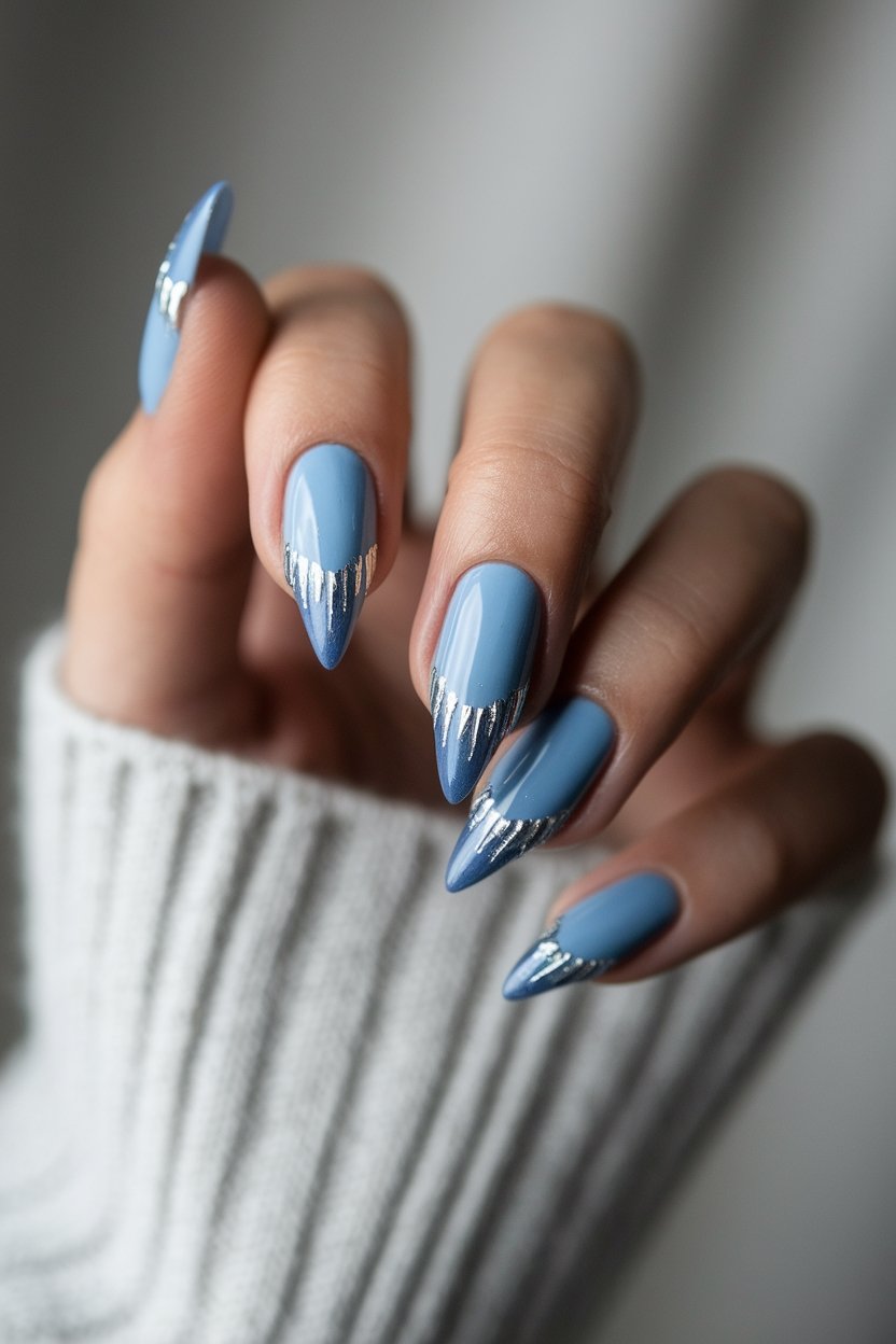 Metallic silver and blue stiletto nails with a cozy gray sweater background.