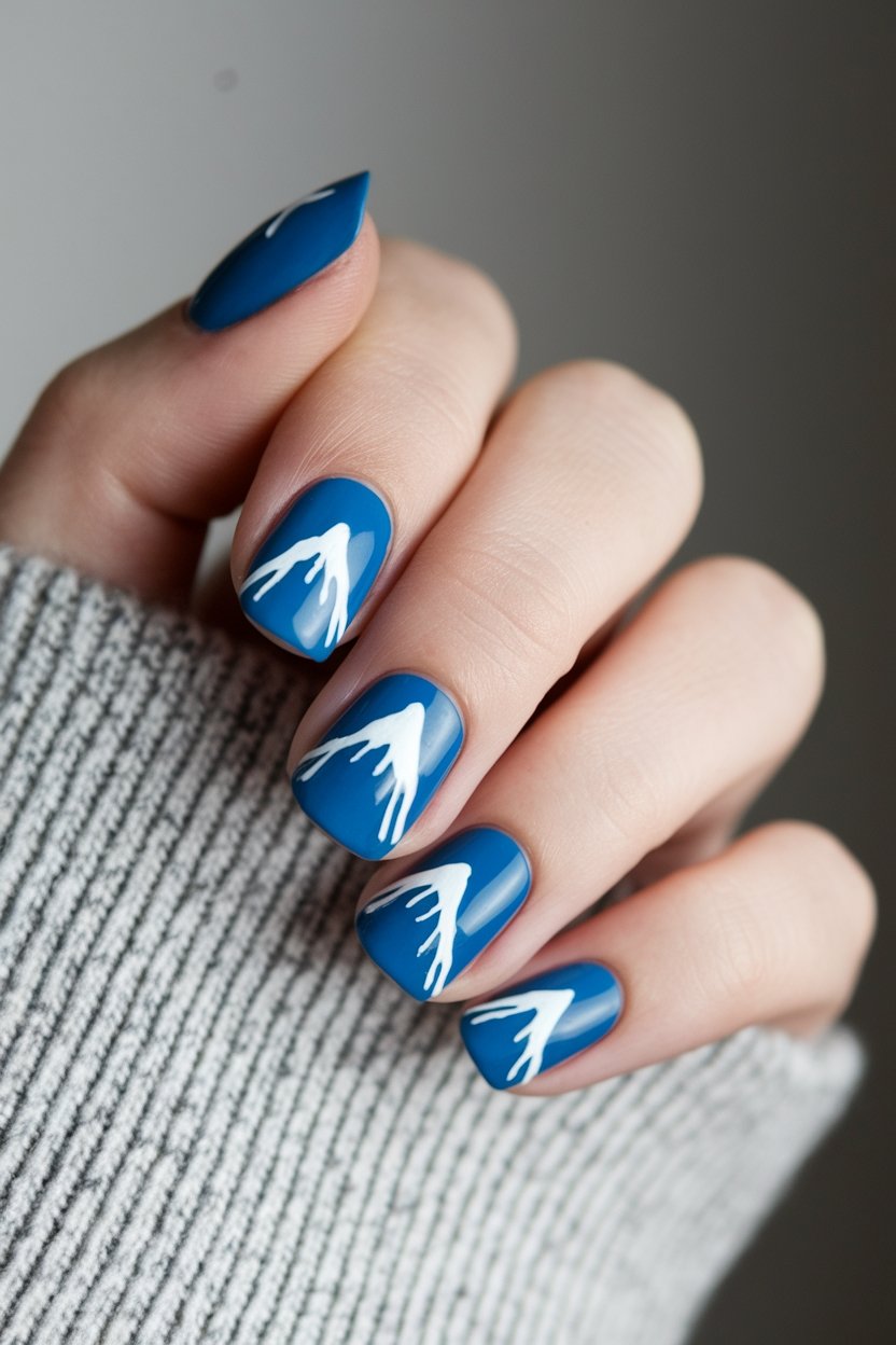 Blue nail art with white mountain-like design on a hand wearing a gray sweater.
