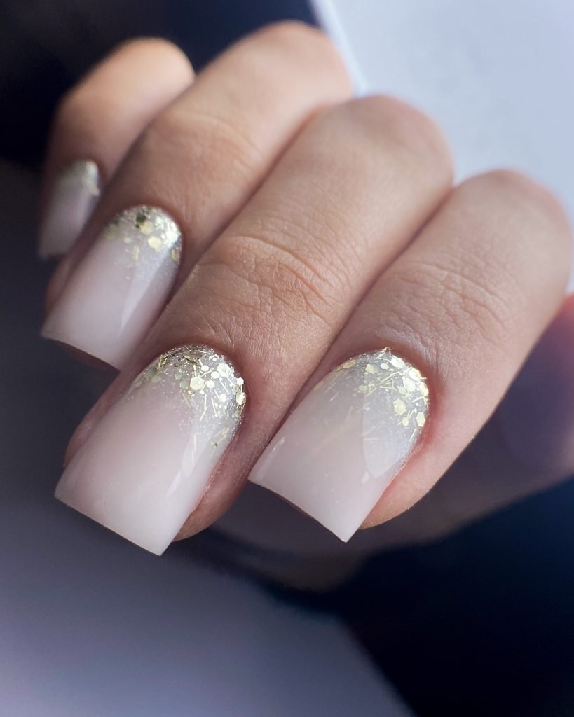 Elegant white ombre nails with gold glitter on natural fingers, showcasing chic manicure design.