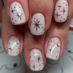 White nails with black starburst and dot designs, featuring a chic and minimalist nail art style.