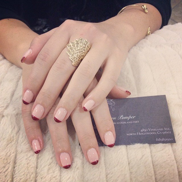 Elegant hands with red-tipped French manicure and a gold ring on a soft fabric background.