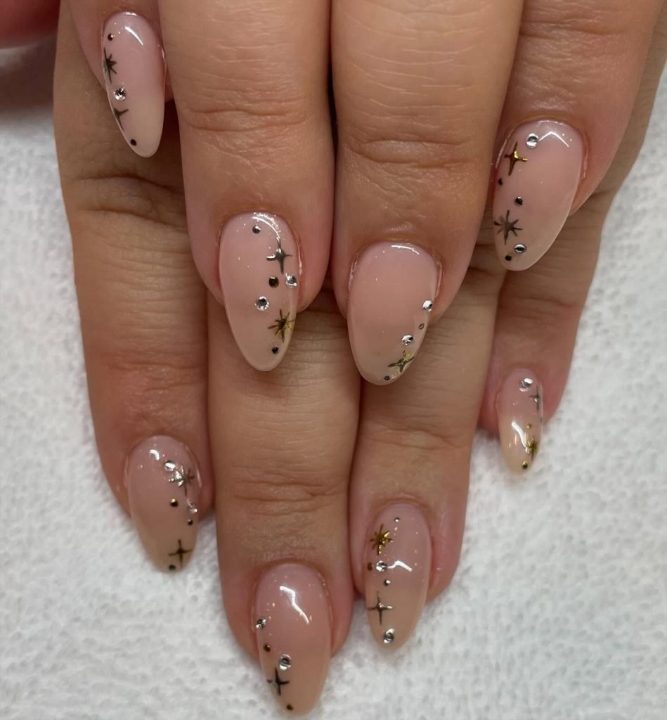 Elegant nude nails with delicate black and gold star designs on a nail art close-up.