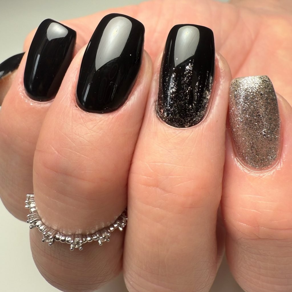 Elegant black and silver glitter manicure with a delicate silver ring, showcasing trendy nail art style.
