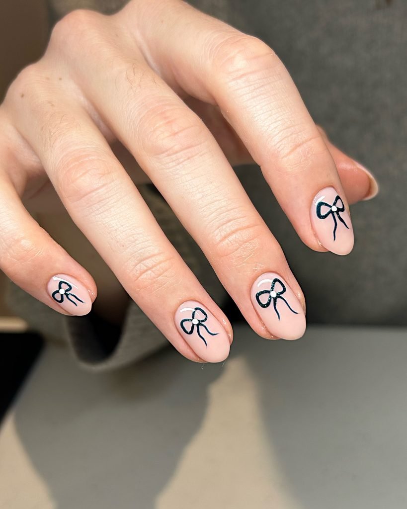 Nude nails with delicate black outlined bow designs, showcasing elegant nail art for a stylish and chic look.