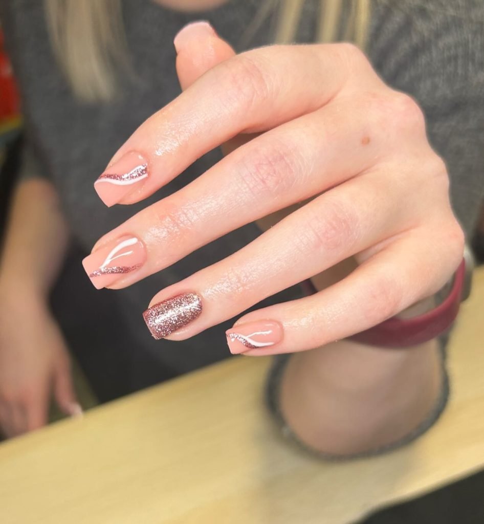 Pink nails with glitter accents and wavy silver lines, showcasing a stylish manicure design.