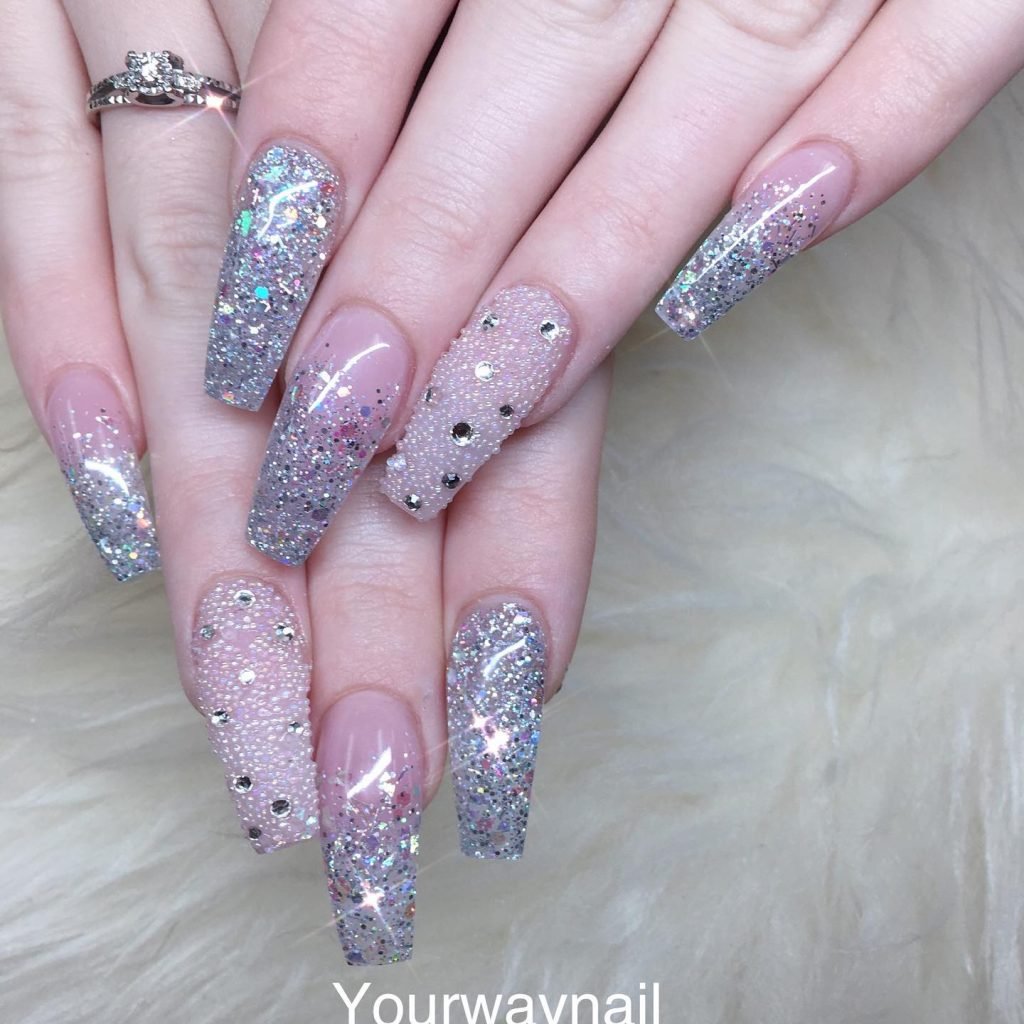 Glittery stiletto nails adorned with rhinestones and a sparkling silver finish on a soft background.
