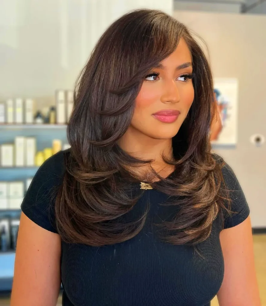 Beautiful woman with styled, layered hair and soft bangs, wearing a black top, in a salon setting.