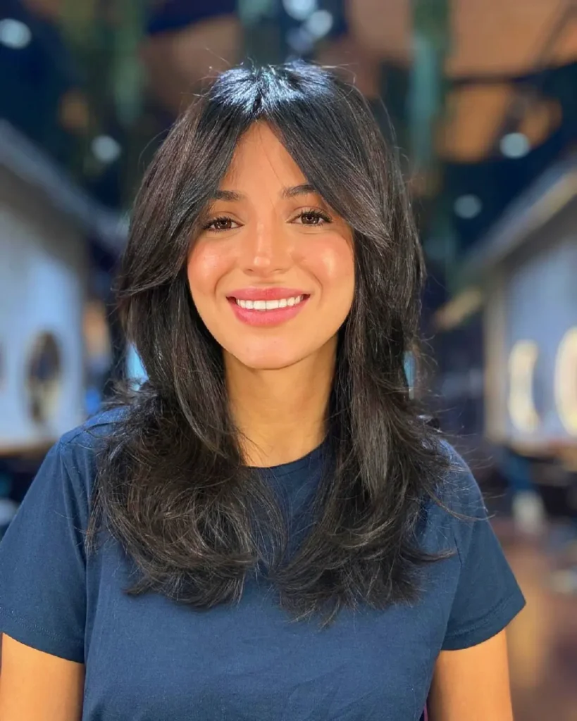 Smiling woman with long, dark hair, wearing a navy shirt, in a stylish indoor setting. Perfect for hair and beauty themes.